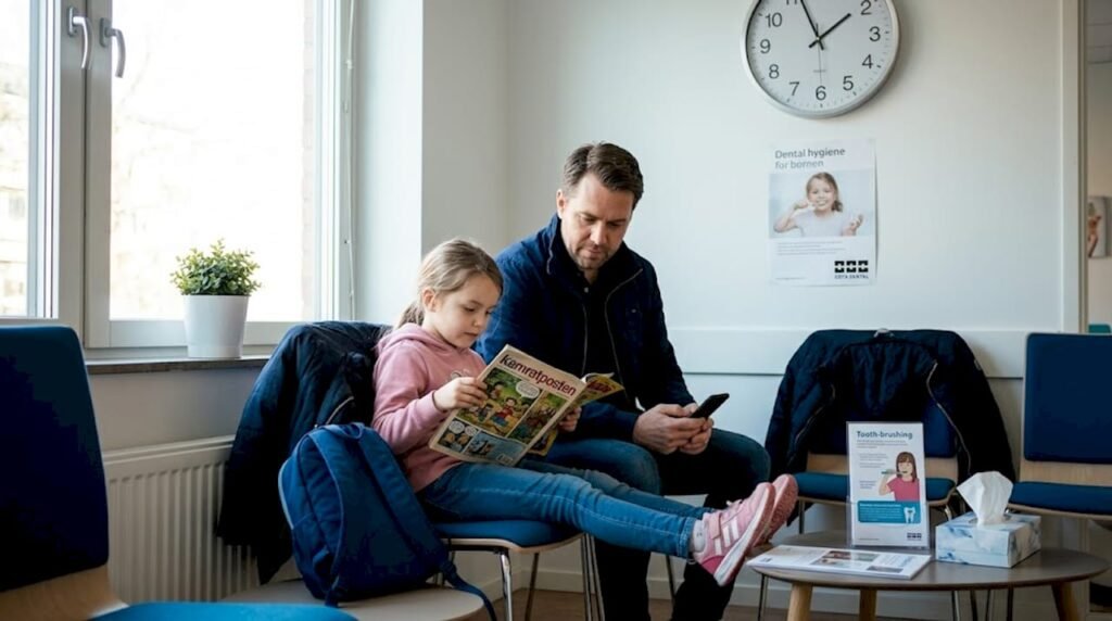 En pappa sitter med sitt barn i väntrummet och väntar på att det ska bli deras tur hos tandläkaren.