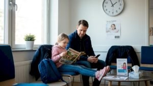 En pappa sitter med sitt barn i väntrummet och väntar på att det ska bli deras tur hos tandläkaren.